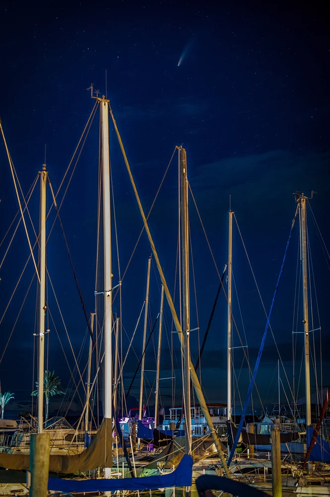Comet Neowise visible above sailboats in a marina at night.