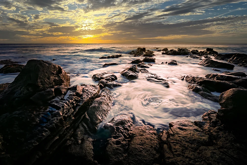Twilight view of rocky shoreline with gentle waves and colorful sky.