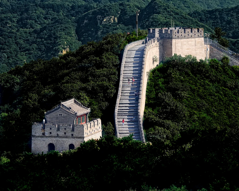 Scenic view of the Great Wall of China winding through lush hills with visitors.