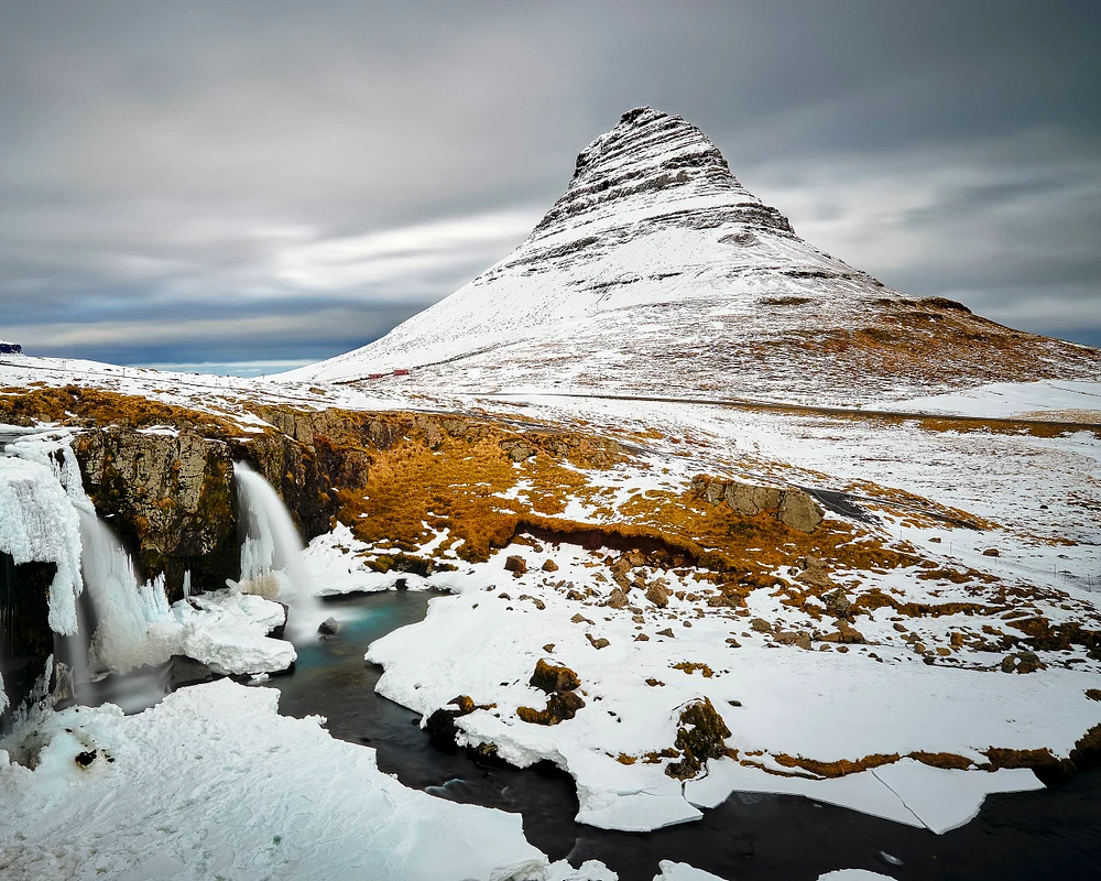 Kirkjufell Mountain with cascading waterfalls and dramatic winter sky.
