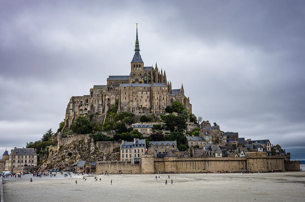 Mont-Saint-Michel island rising from the Normandy coast under a cloudy sky.