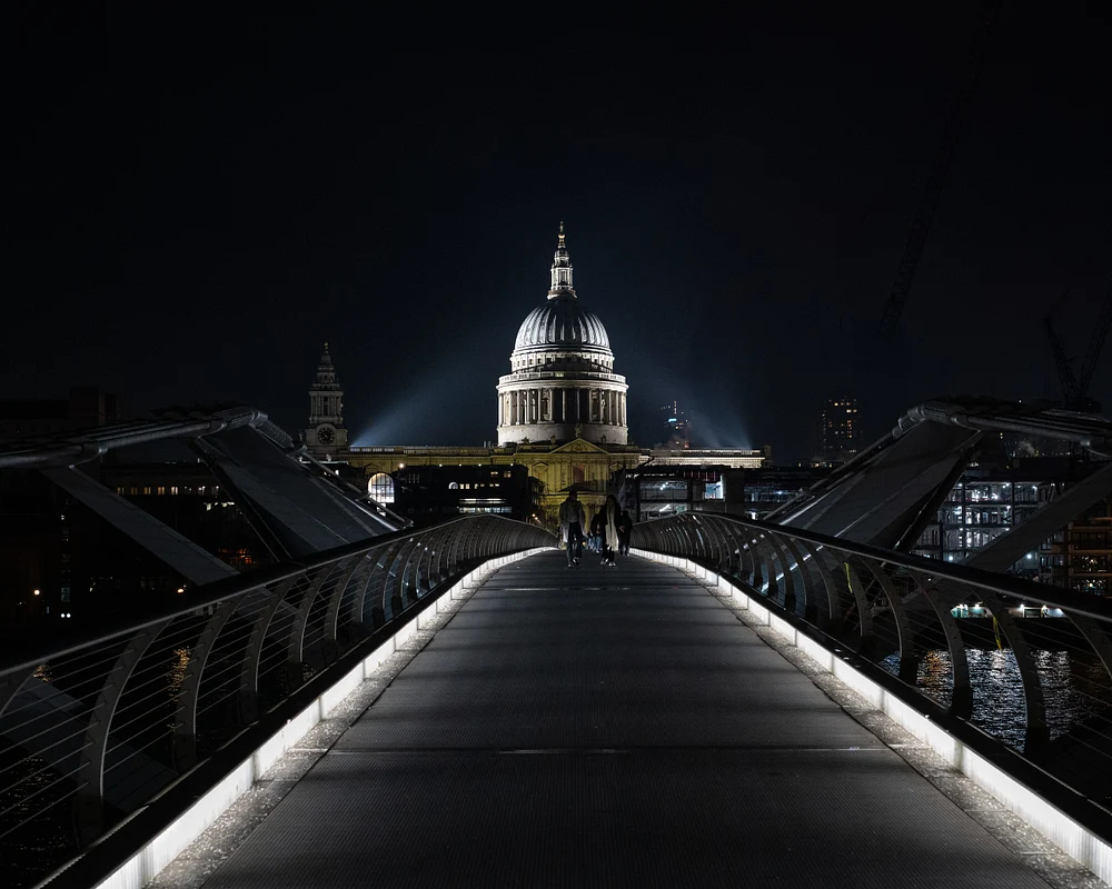 Millennium Bridge illuminated at night with St. Paul's Cathedral in the background, showcasing a romantic city scene.