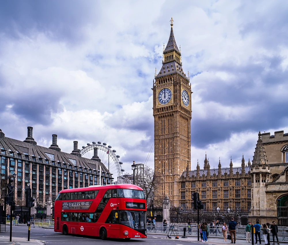 Big Ben clock tower with a red double-decker bus and London Eye in the background.