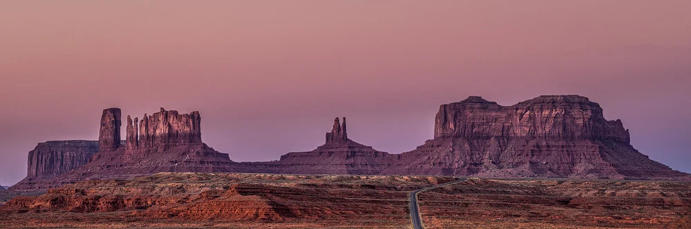 Monument Valley landscape at dusk with red rock formations and winding road.