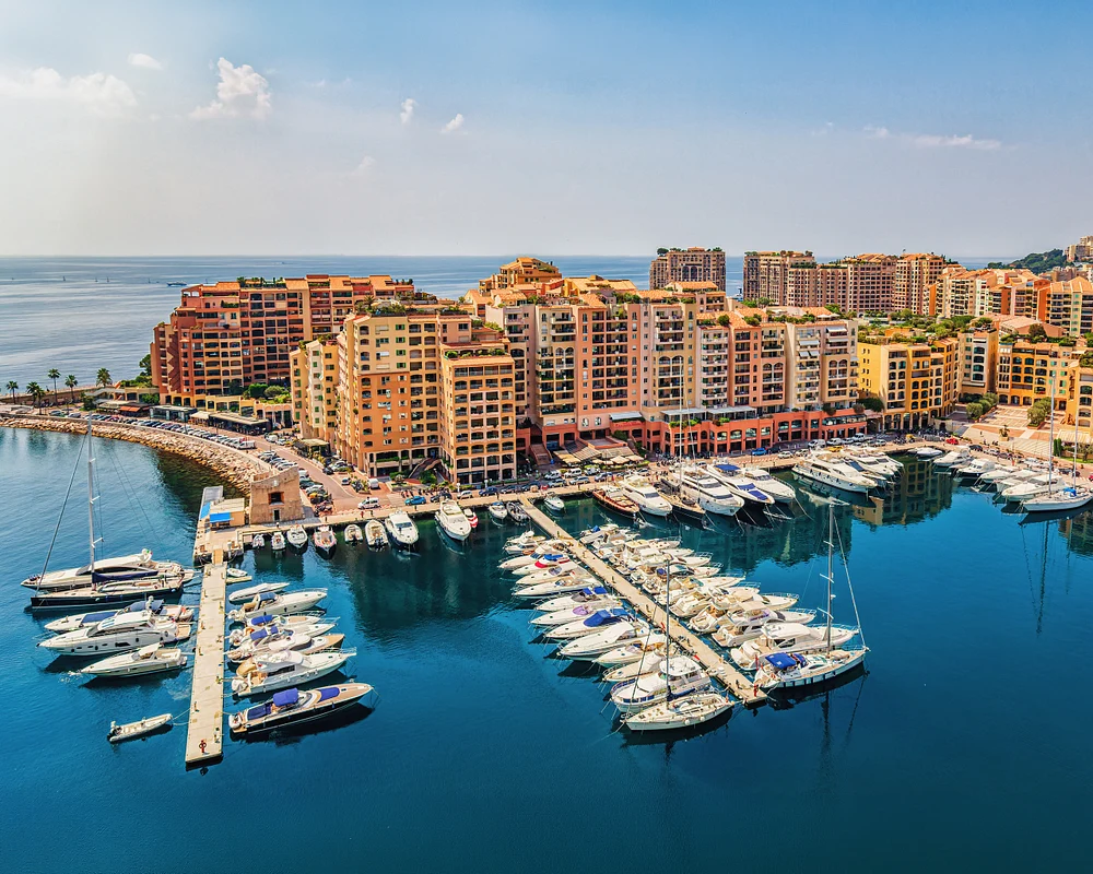 Aerial view of Monaco&rsquo;s Fontvieille marina, with yachts below colorful waterfront apartments and open sea beyond