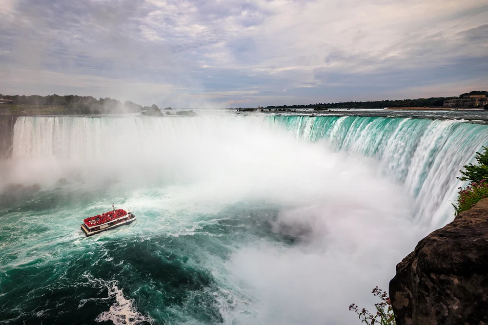 Tour boat nears Niagara&rsquo;s Horseshoe Falls as turquoise water crashes through dense rising spray