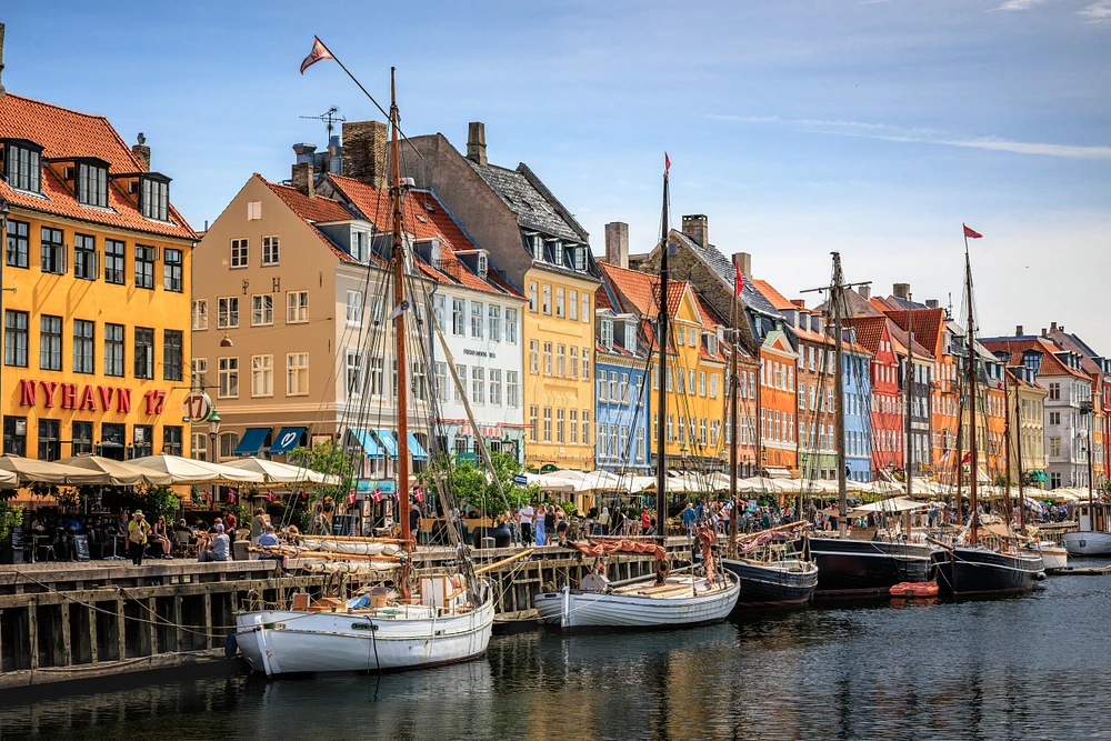 Colorful Copenhagen townhouses and moored sailing vessels line Nyhavn harbor beneath a clear blue sky