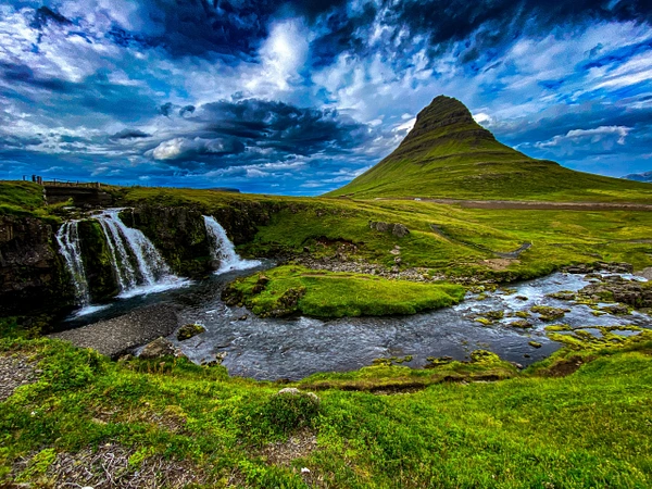 A picturesque view of Kirkjufell mountain with a waterfall in the foreground under dramatic skies.