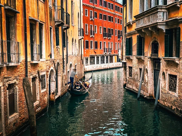 A gondola navigates a narrow canal in Venice with colorful buildings lining the banks.