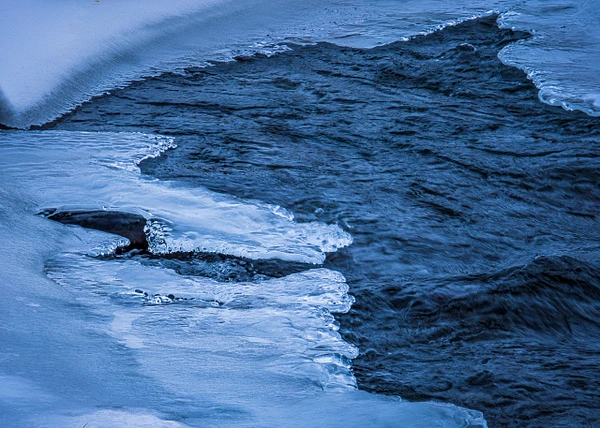 A close-up view of an icy shoreline with flowing water underneath.