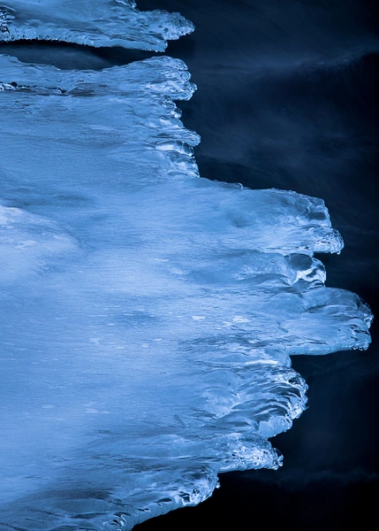 Close-up of intricate frozen waves in deep blue tones against a dark background.