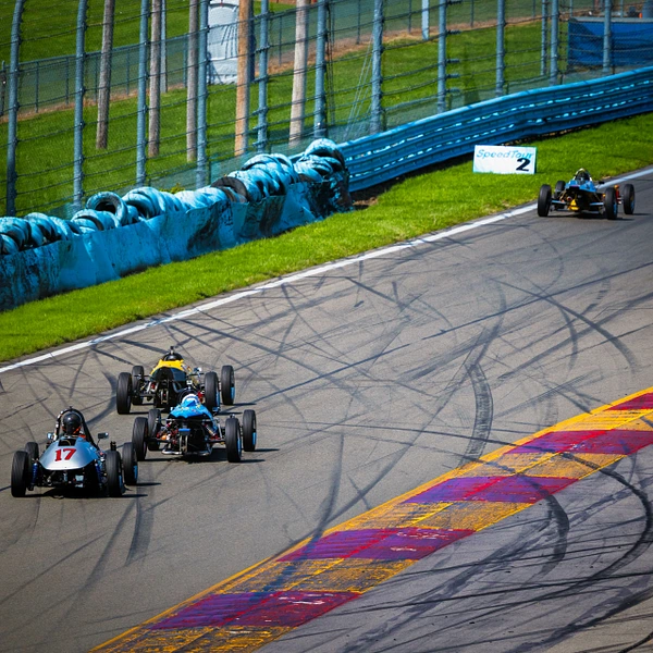 Three formula cars racing at Watkins Glen International with vibrant track colors.