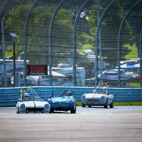 Three classic sports cars racing at Watkins Glen International track.