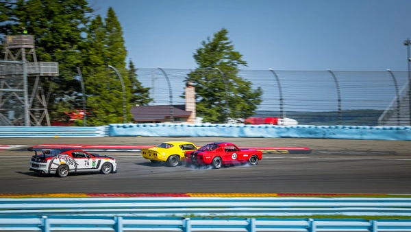 Three classic race cars competing on the track at Watkins Glen International.