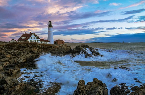 Portland Head Light lighthouse at sunrise with gentle waves on rocky shore.