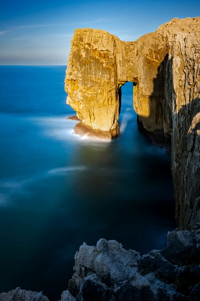 Coastal arch illuminated by sunset with calm ocean waters.
