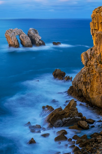 Sunset view at Playa de Portio, Spain, featuring dramatic cliffs and tranquil waters.