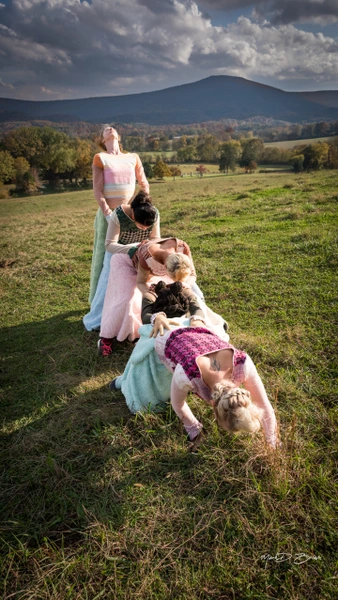 Dancers in colorful costumes performing in a grassy field with mountains in the background.